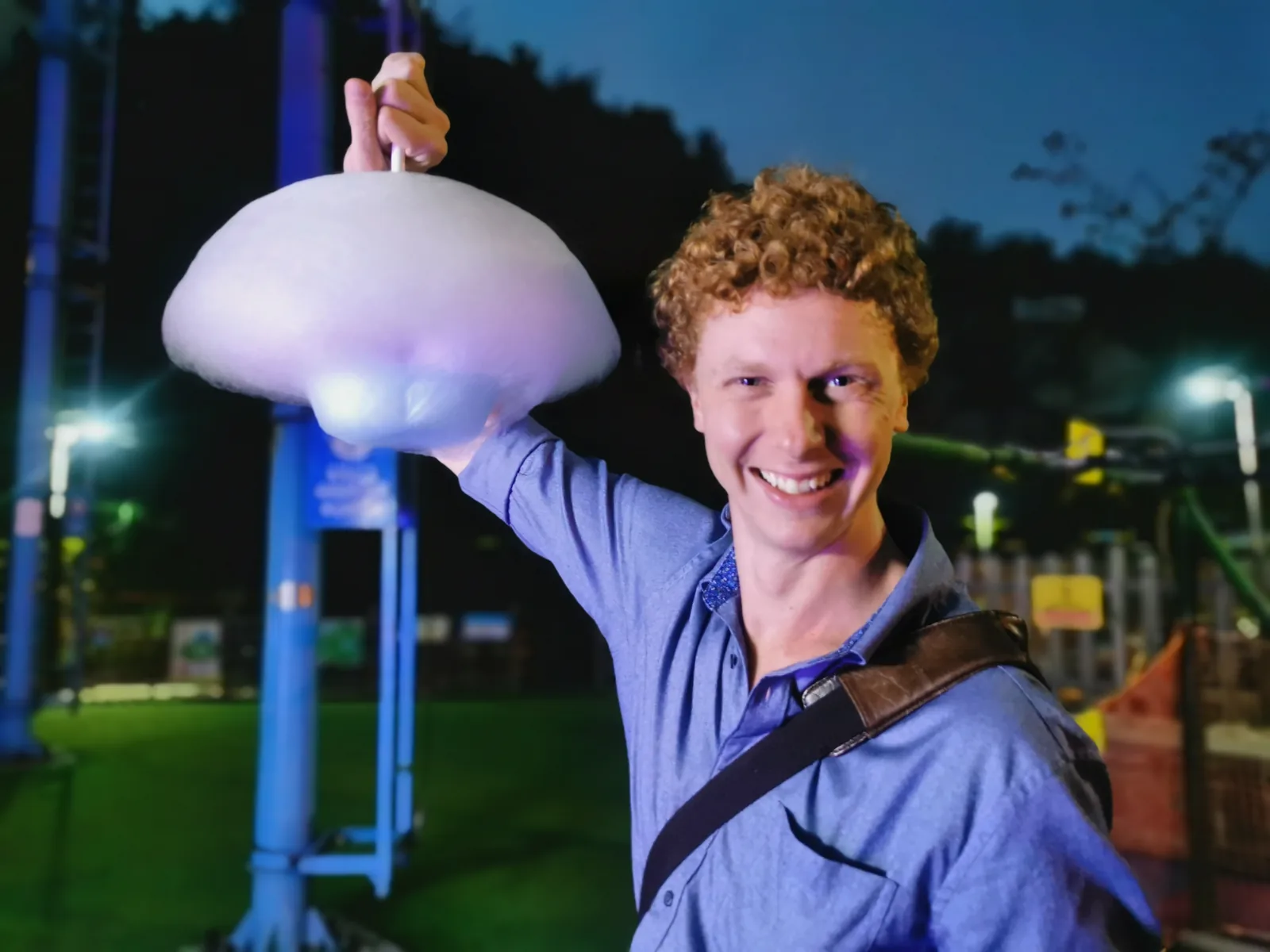 Customer holding a large cloud of cotton candy next to a vending machine at night